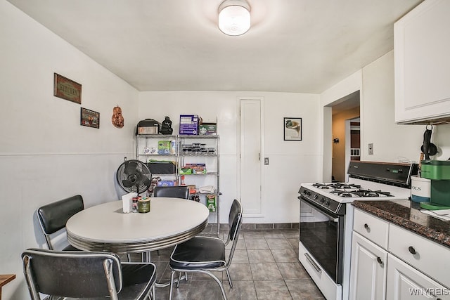 kitchen featuring light tile patterned floors, dark stone counters, white cabinetry, and white gas stove