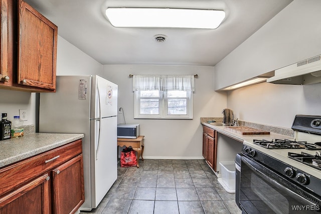 kitchen featuring exhaust hood, white refrigerator, sink, gas range oven, and light tile patterned flooring