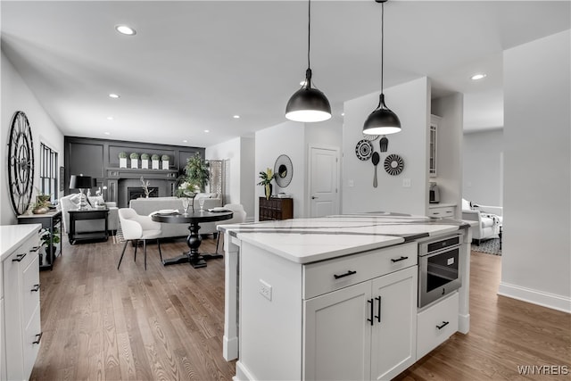 kitchen featuring light stone countertops, stainless steel oven, light hardwood / wood-style floors, white cabinetry, and hanging light fixtures