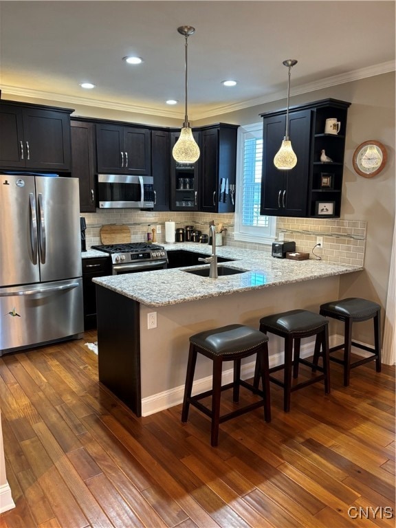 kitchen with kitchen peninsula, a breakfast bar, stainless steel appliances, dark wood-type flooring, and hanging light fixtures