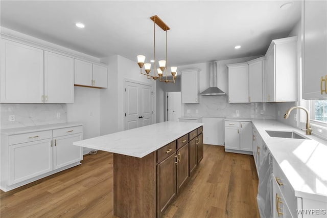 kitchen featuring white cabinetry, sink, wall chimney range hood, light hardwood / wood-style flooring, and a kitchen island