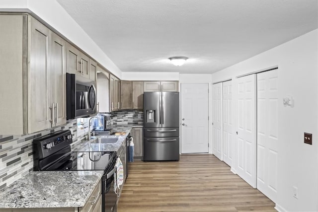 kitchen with backsplash, sink, hardwood / wood-style flooring, appliances with stainless steel finishes, and light stone counters