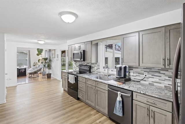 kitchen featuring light stone countertops, appliances with stainless steel finishes, decorative backsplash, sink, and light hardwood / wood-style flooring