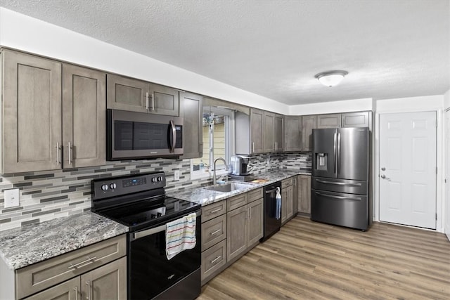 kitchen with decorative backsplash, light stone counters, sink, black appliances, and wood-type flooring