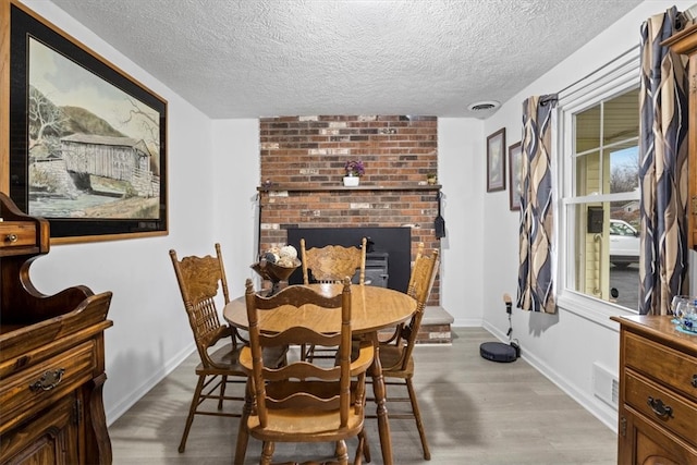 dining space featuring a fireplace, light hardwood / wood-style flooring, and a textured ceiling