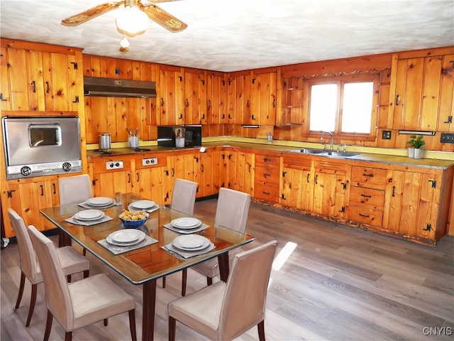 kitchen featuring stainless steel appliances, ceiling fan, sink, light hardwood / wood-style flooring, and wood walls