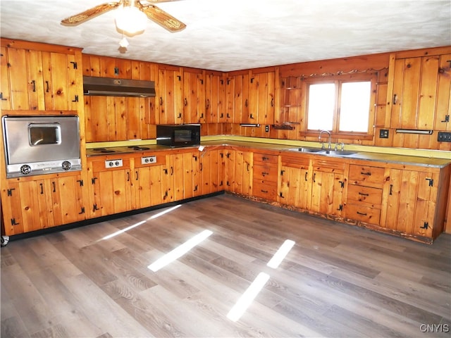 kitchen with ceiling fan, sink, dark wood-type flooring, and wooden walls