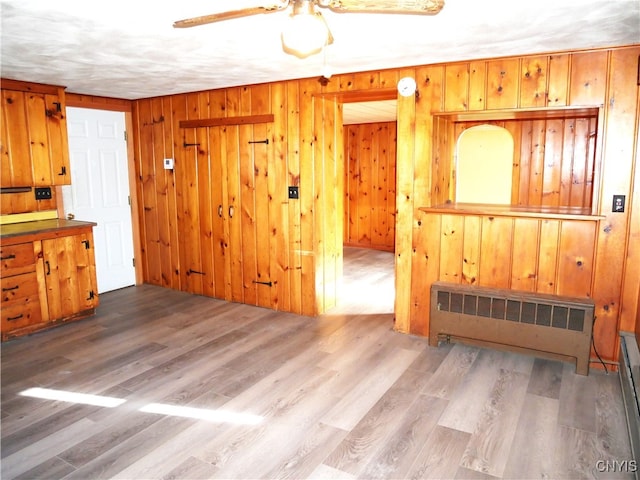 living room featuring radiator, wooden walls, ceiling fan, and light wood-type flooring