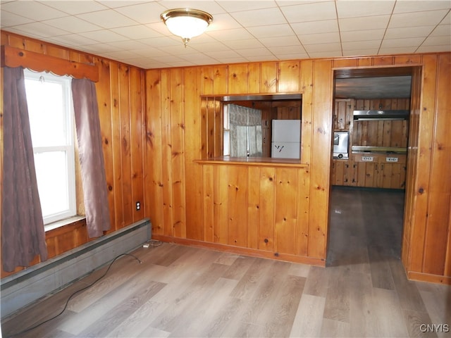 unfurnished room featuring hardwood / wood-style flooring, a baseboard radiator, and wood walls