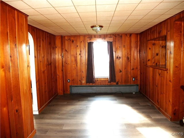 empty room featuring dark hardwood / wood-style flooring, baseboard heating, and wood walls