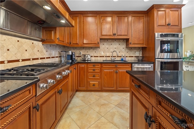 kitchen with appliances with stainless steel finishes, tasteful backsplash, wall chimney range hood, sink, and light tile patterned floors