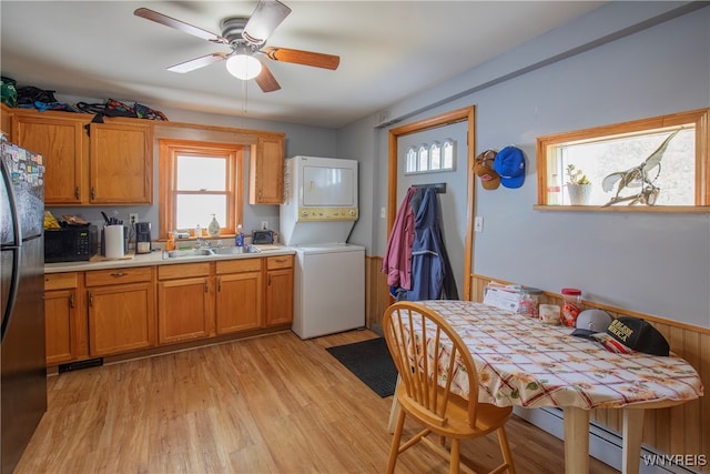 kitchen featuring sink, stacked washer and dryer, light hardwood / wood-style flooring, ceiling fan, and stainless steel refrigerator