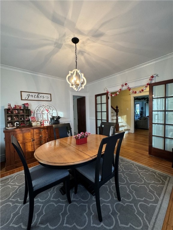 dining space with wood-type flooring, an inviting chandelier, french doors, and crown molding