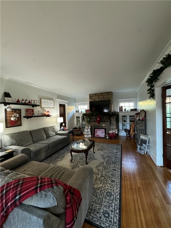 living room with wood-type flooring, a stone fireplace, and crown molding