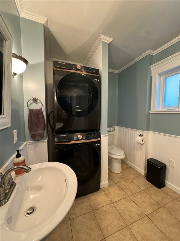 bathroom with crown molding, sink, tile patterned flooring, stacked washer and dryer, and toilet