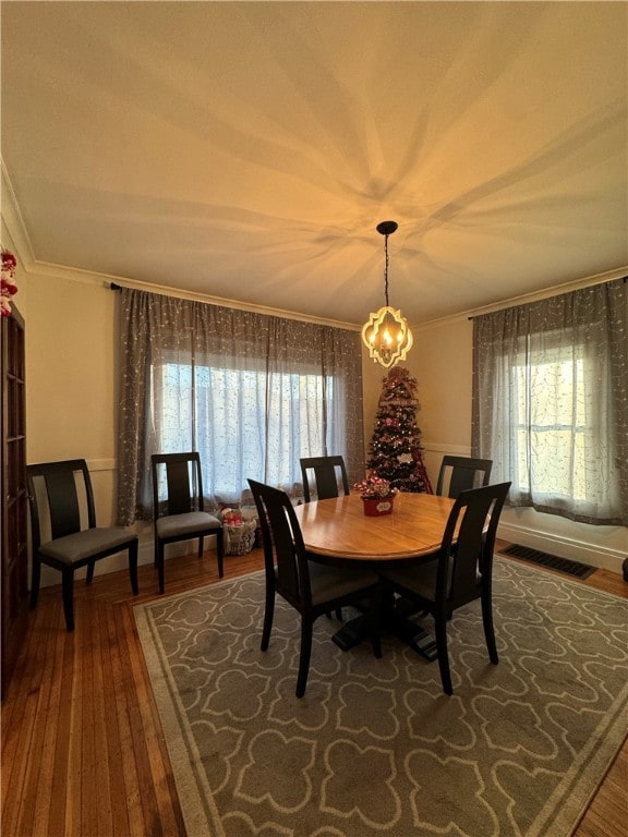 dining space featuring wood-type flooring, ornamental molding, and a notable chandelier