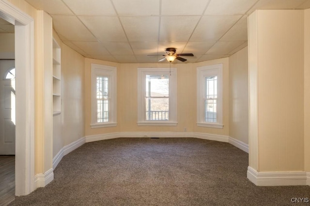 spare room with a paneled ceiling, ceiling fan, built in features, and dark colored carpet