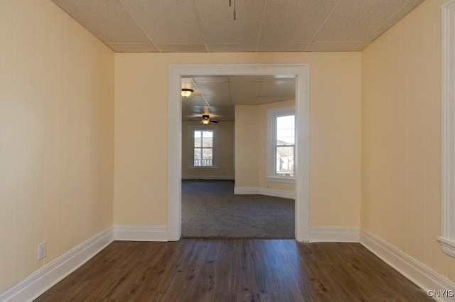 empty room with a paneled ceiling, ceiling fan, and dark hardwood / wood-style flooring