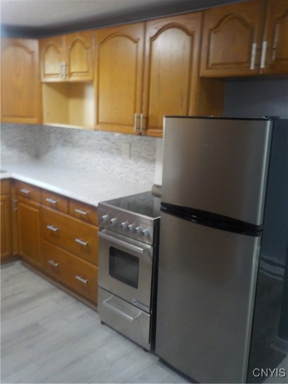 kitchen with appliances with stainless steel finishes, light hardwood / wood-style floors, and tasteful backsplash