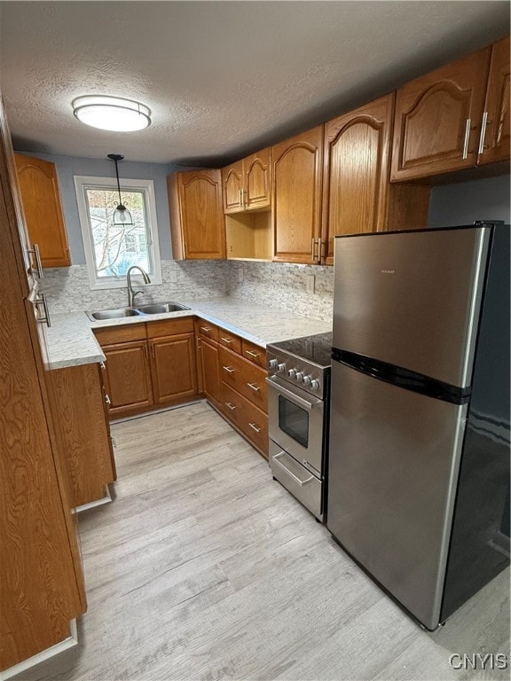 kitchen featuring decorative backsplash, appliances with stainless steel finishes, sink, decorative light fixtures, and light hardwood / wood-style floors