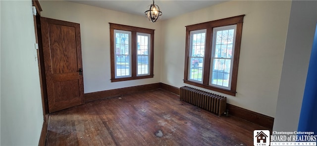 empty room featuring radiator heating unit, dark wood-type flooring, and an inviting chandelier