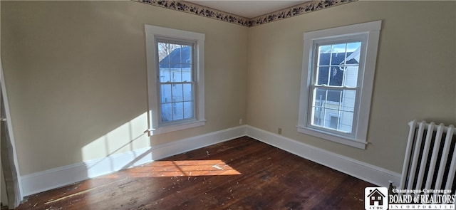 empty room featuring a healthy amount of sunlight, dark wood-type flooring, and radiator