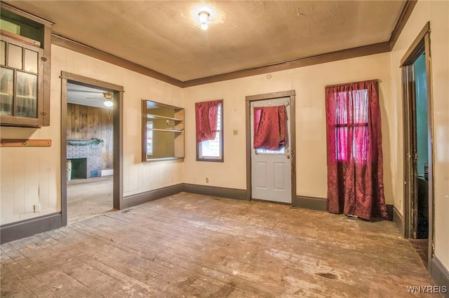 foyer entrance with wooden walls, a brick fireplace, ceiling fan, ornamental molding, and wood-type flooring