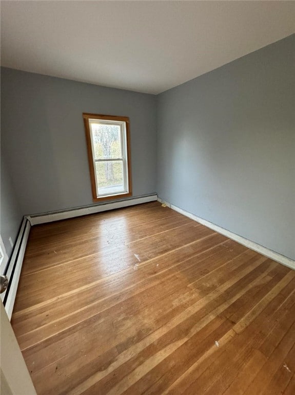 empty room featuring a baseboard heating unit and hardwood / wood-style flooring