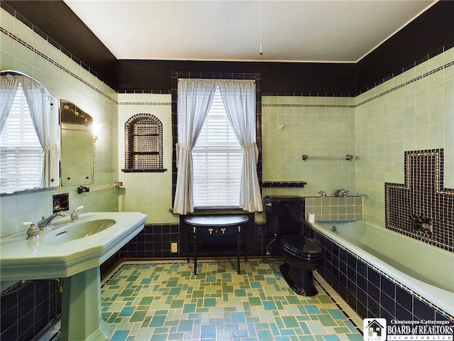 bathroom featuring toilet, tile walls, a wealth of natural light, and tiled bath