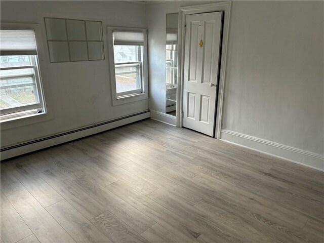 empty room featuring plenty of natural light, light wood-type flooring, and a baseboard heating unit