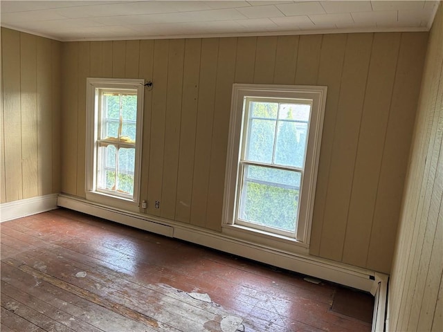 unfurnished room with dark wood-type flooring, plenty of natural light, a baseboard heating unit, and wood walls