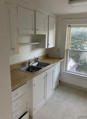 kitchen with light floors, baseboards, white cabinetry, and a sink