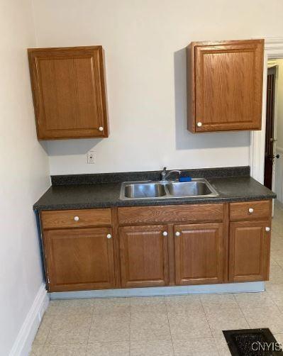 kitchen with brown cabinets, dark countertops, baseboards, and a sink