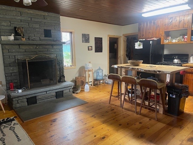 interior space featuring a breakfast bar, wooden ceiling, black fridge, a stone fireplace, and light hardwood / wood-style floors