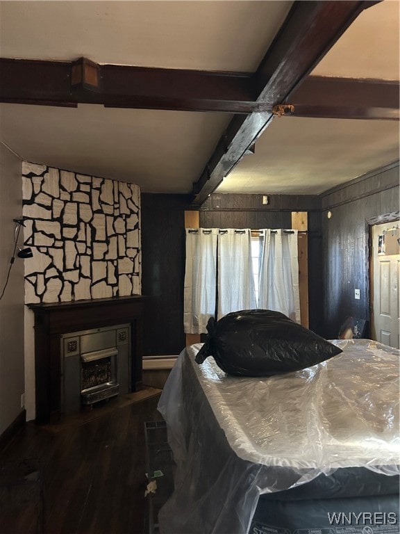 bedroom with hardwood / wood-style floors, wooden walls, a fireplace, a baseboard radiator, and beamed ceiling