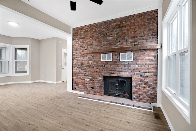 unfurnished living room with ceiling fan, light wood-type flooring, a wealth of natural light, and a brick fireplace