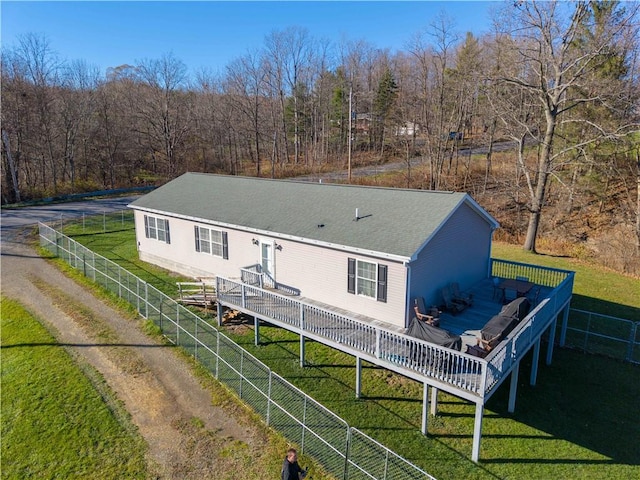 rear view of property featuring roof with shingles, a yard, a wooden deck, and fence