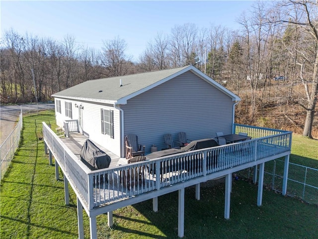 rear view of property with a deck, a yard, a shingled roof, and fence