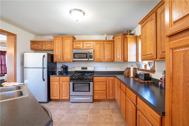 kitchen featuring stainless steel appliances, dark countertops, brown cabinets, and a sink