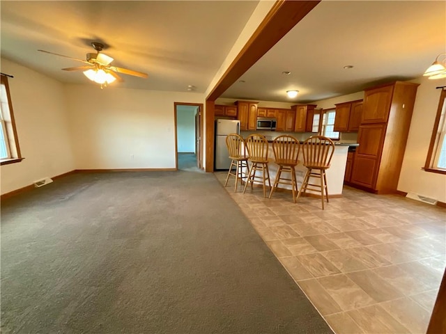 kitchen with visible vents, stainless steel microwave, brown cabinets, a breakfast bar, and freestanding refrigerator