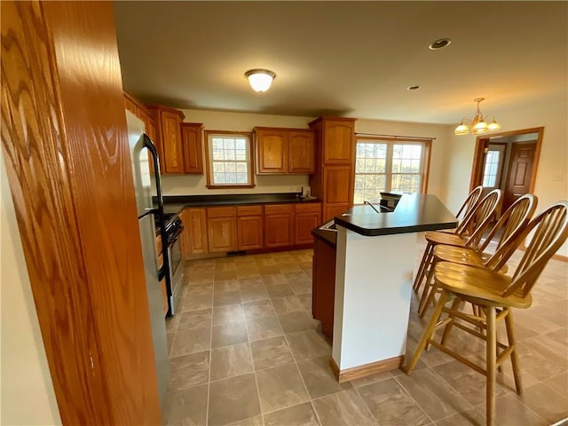 kitchen featuring stainless steel gas range oven, a breakfast bar area, dark countertops, and a wealth of natural light