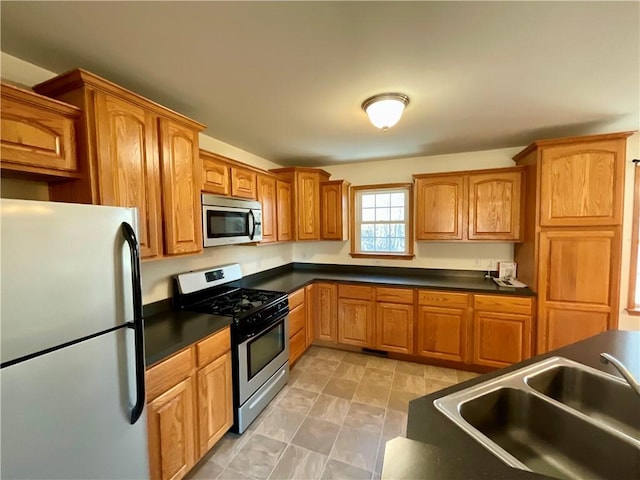 kitchen with stainless steel appliances, brown cabinetry, dark countertops, and a sink