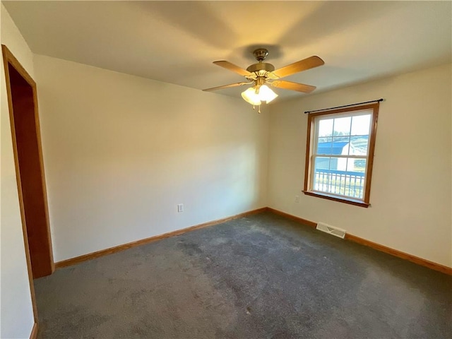 empty room featuring a ceiling fan, dark colored carpet, visible vents, and baseboards