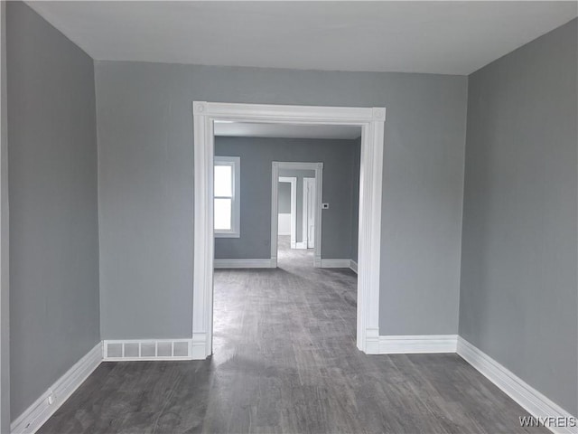 empty room with dark wood finished floors, visible vents, and baseboards