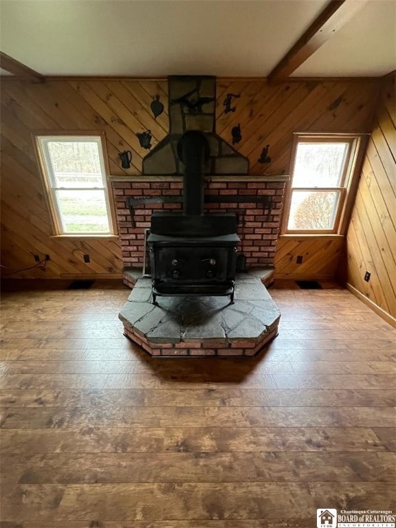 unfurnished living room featuring beam ceiling, a wood stove, plenty of natural light, and wood walls