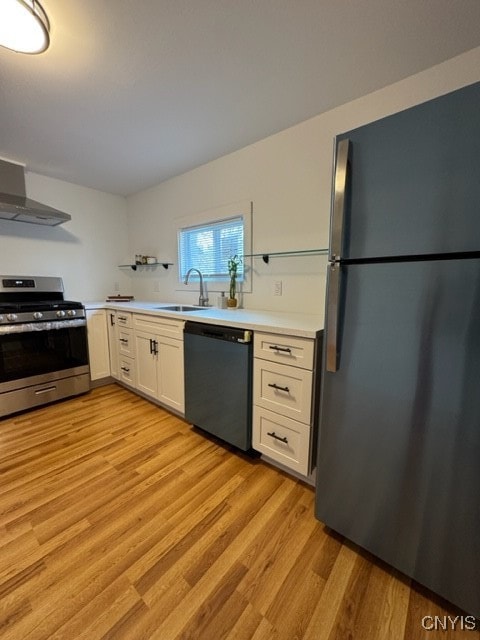 kitchen featuring sink, stainless steel appliances, wall chimney range hood, light hardwood / wood-style flooring, and white cabinets