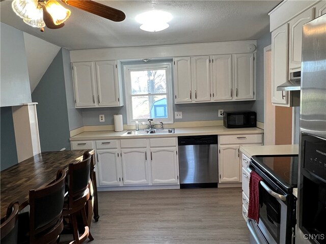 kitchen with sink, stainless steel appliances, a textured ceiling, white cabinets, and light wood-type flooring