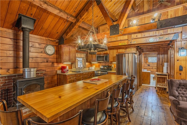 kitchen with a wood stove, sink, stainless steel appliances, lofted ceiling with beams, and wood walls