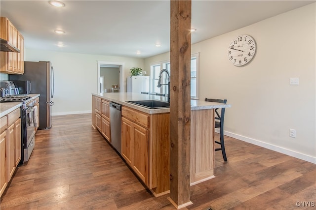 kitchen featuring appliances with stainless steel finishes, a kitchen breakfast bar, a kitchen island with sink, sink, and dark hardwood / wood-style floors