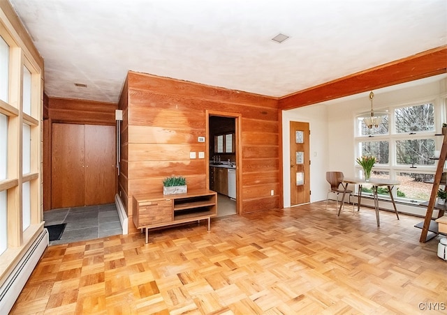 interior space featuring light parquet flooring, an inviting chandelier, baseboard heating, and wooden walls